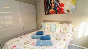 Una camera da letto con una coperta a fiori, un quadro appeso e un letto rifatto con asciugamani blu.