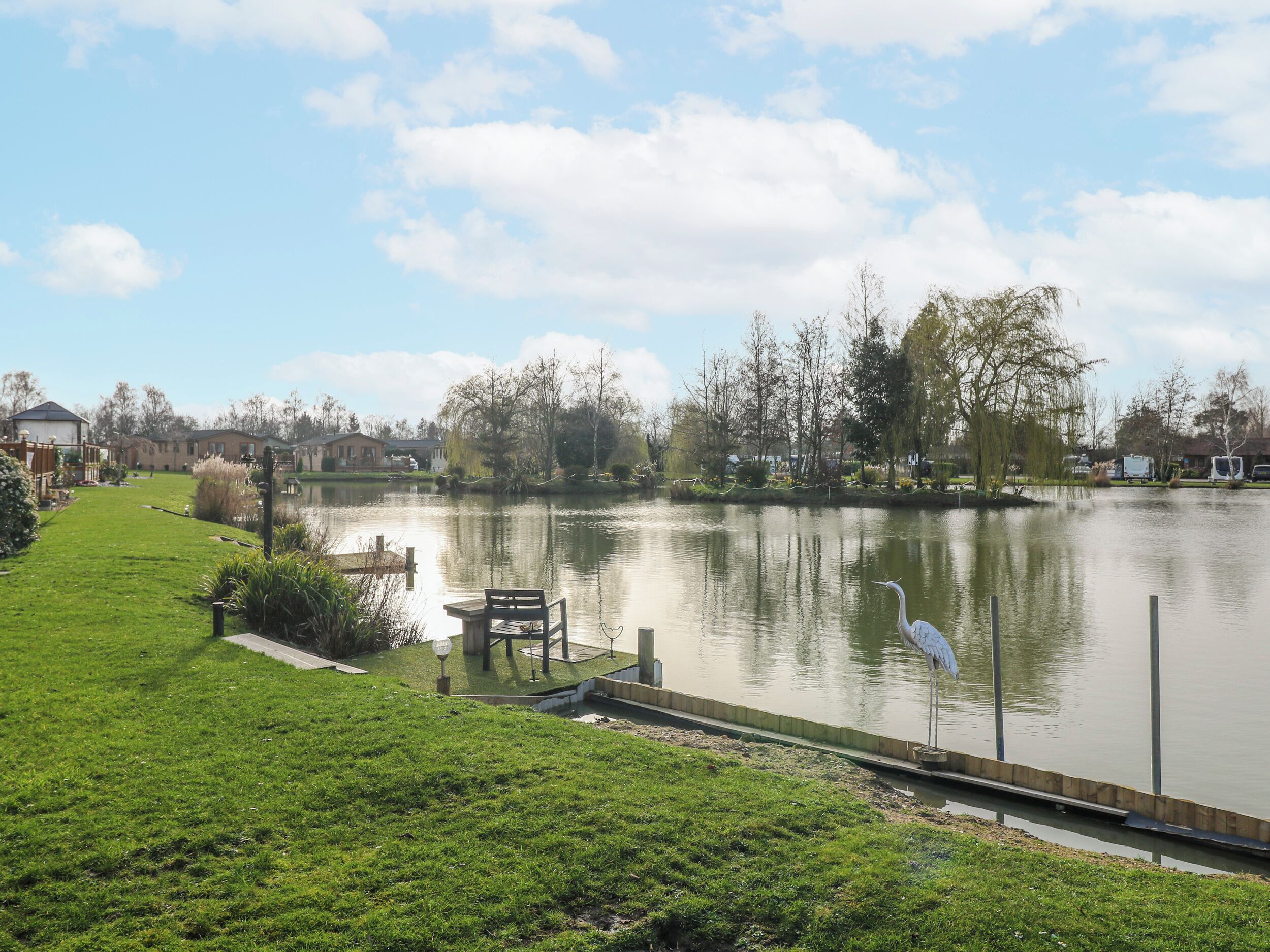 A serene lakeside view with a grassy area, a dock, and a white heron standing by the water.