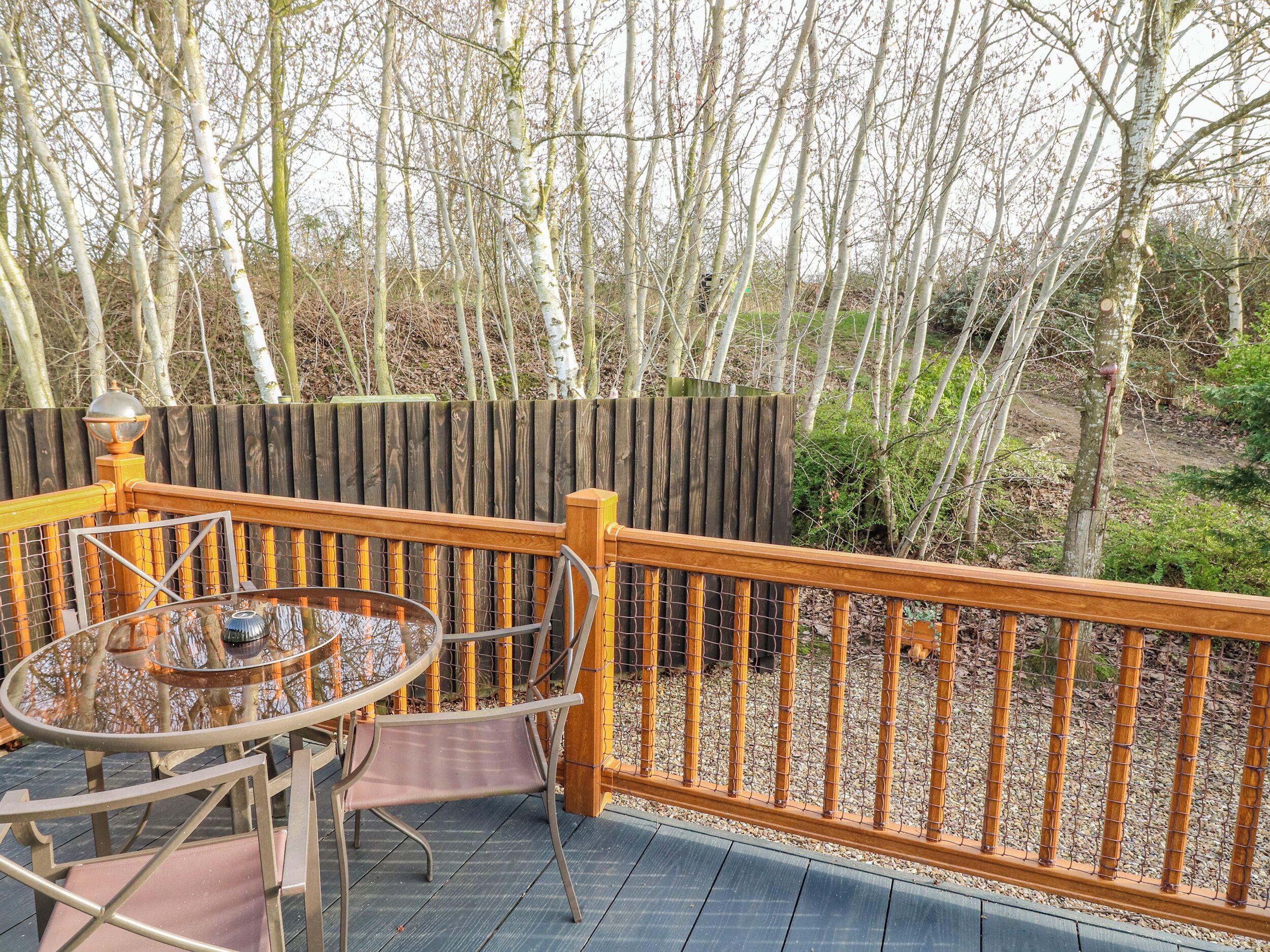A deck with a table and chairs, surrounded by a wooden fence and trees.
