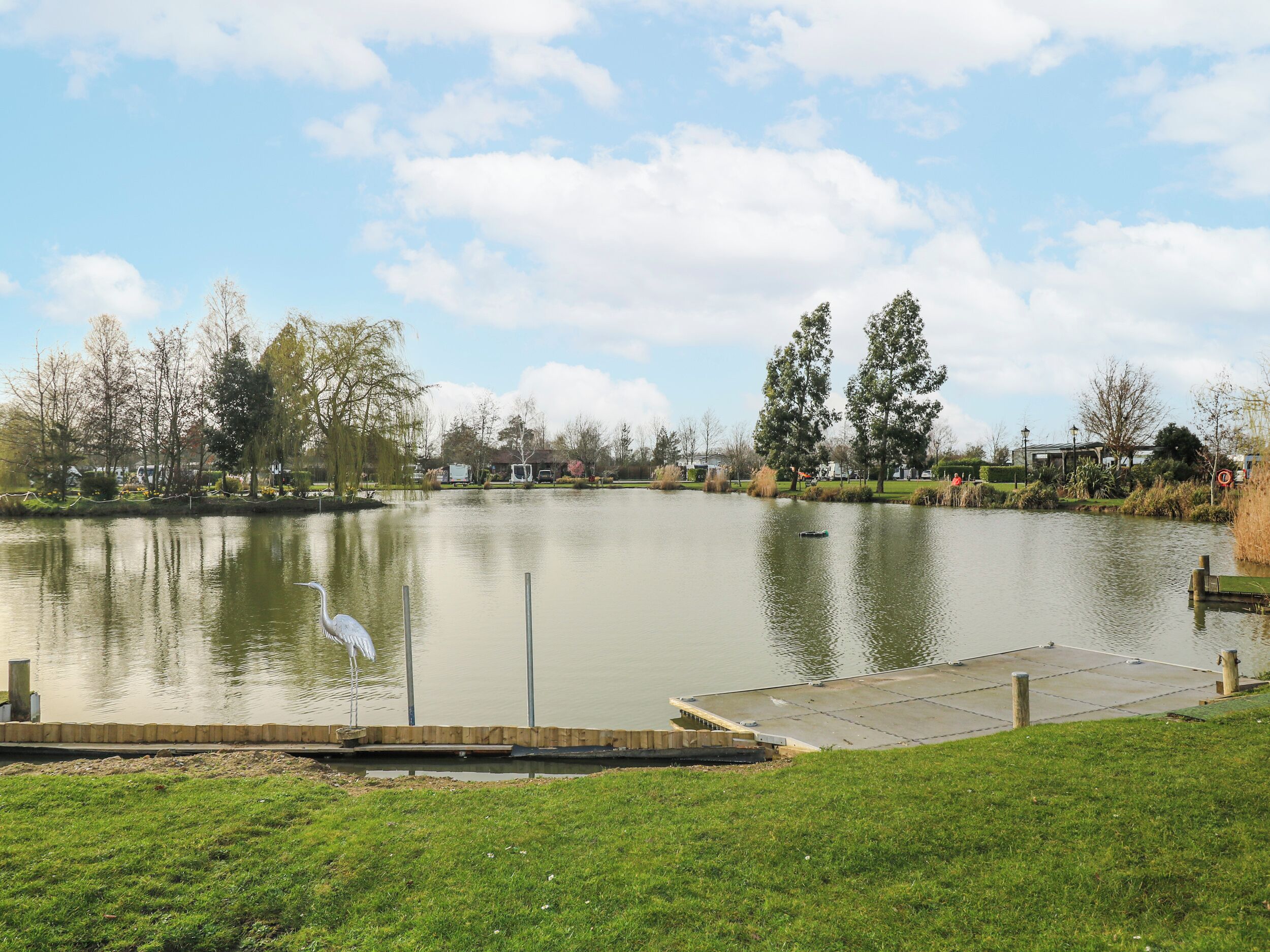 A calm lake with a dock, surrounded by grass and trees.