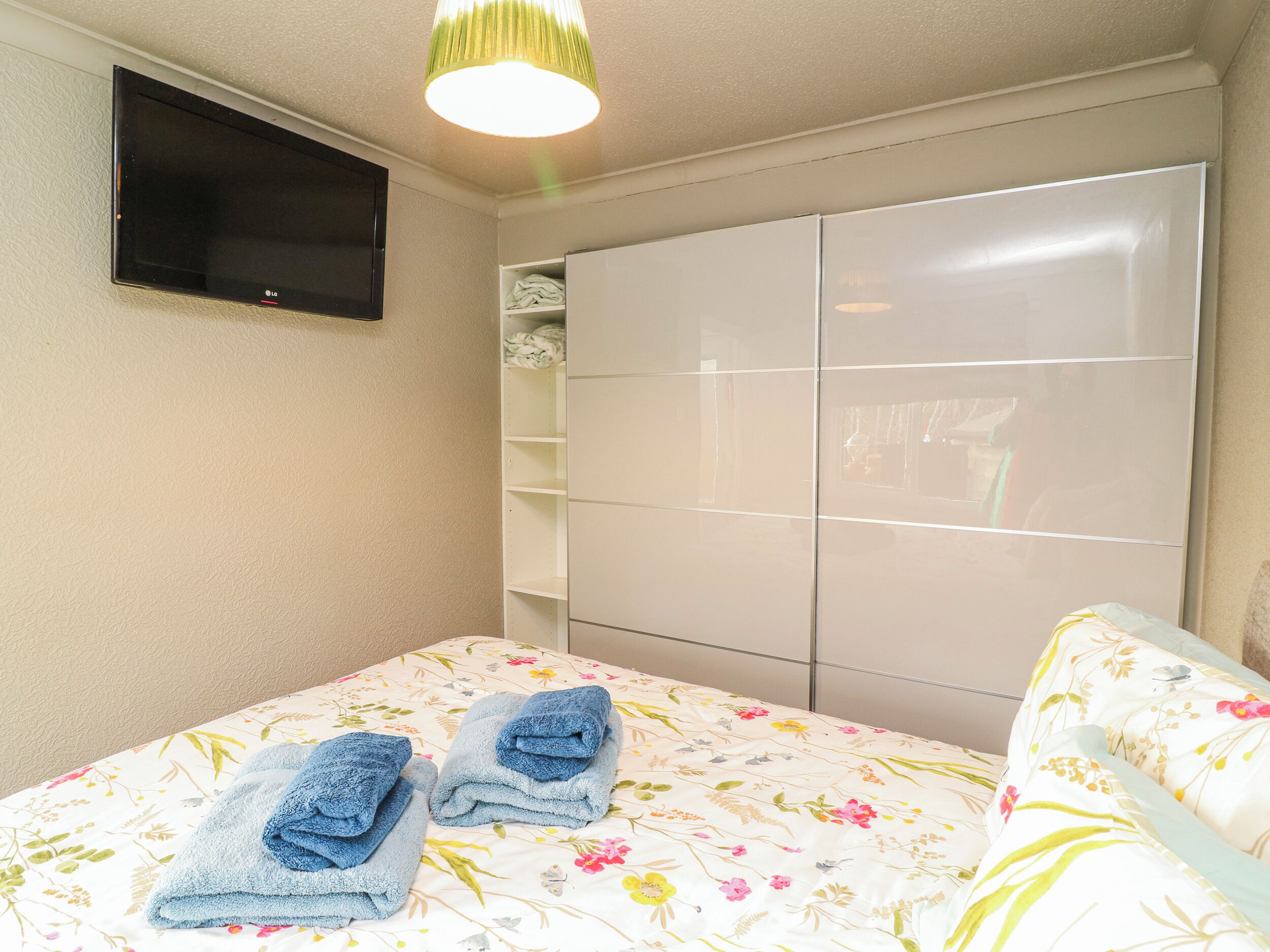 A bedroom with a bed, a TV mounted on the wall, and a wardrobe.
