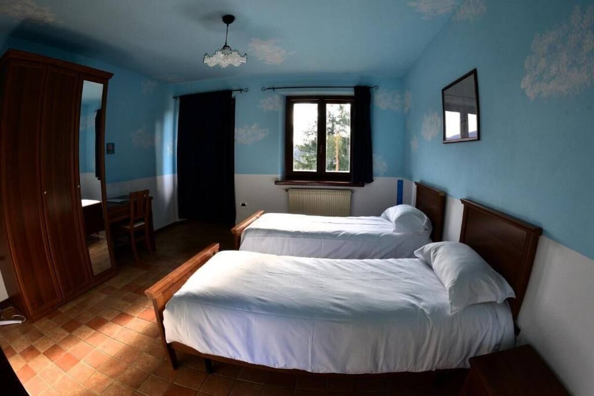 A bedroom with two beds, a window, a radiator, and a wardrobe.