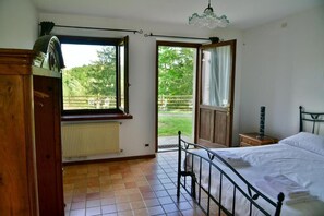 A bedroom with a bed, a window, a radiator, and a view of a garden. - Tenuta Valdomini (Attimis)