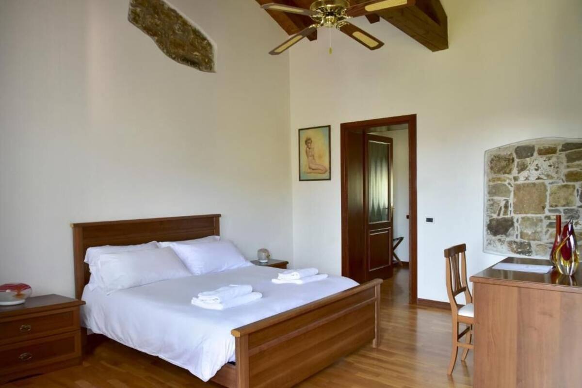 A bedroom with a wooden bed, a nightstand, a desk, and a chair.