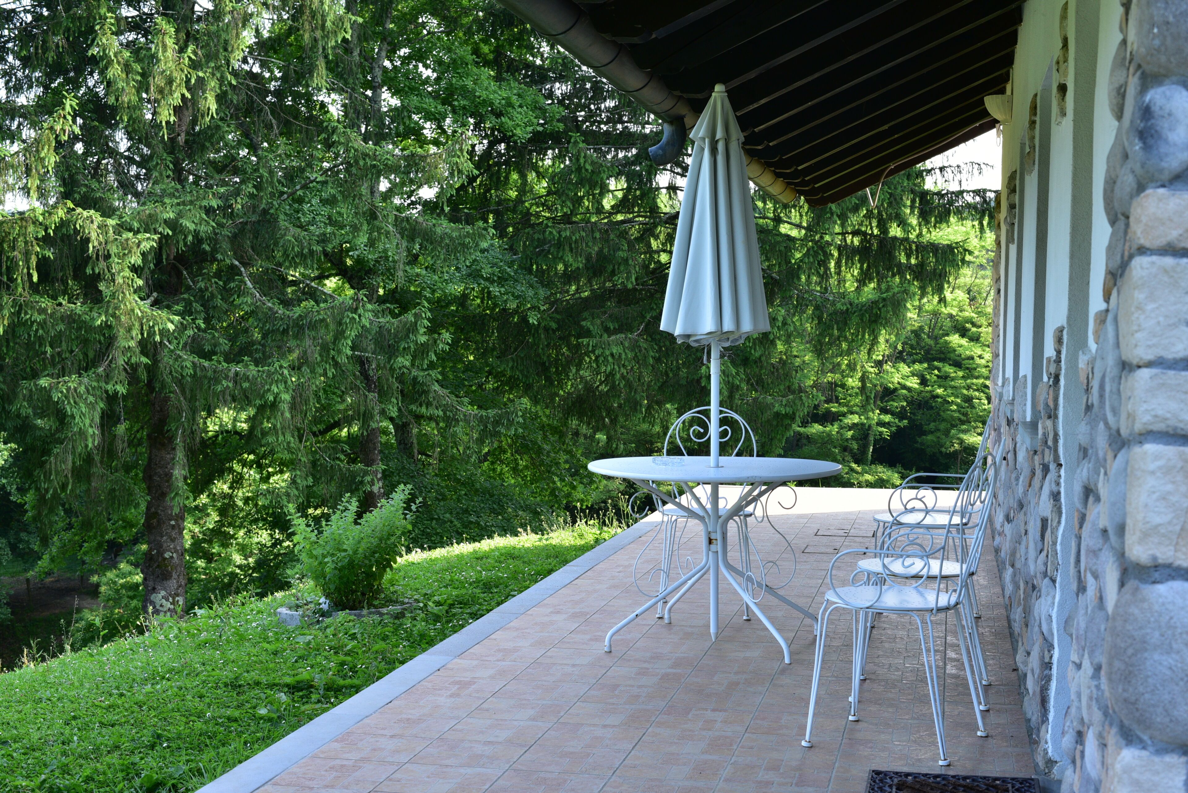 Patio esterno con tavolo e sedie, immerso nel verde e delimitato da un muro in pietra.