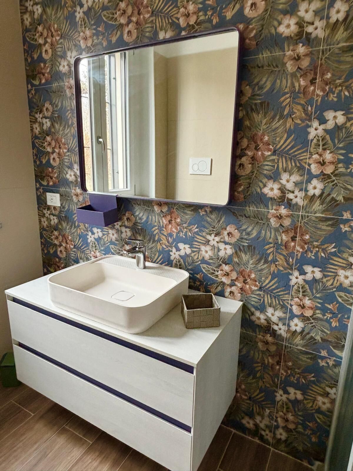 A bathroom with a white vanity, a rectangular mirror, and floral-patterned tiles.