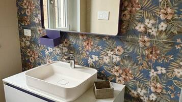 A bathroom with a white vanity, a rectangular mirror, and floral-patterned tiles.