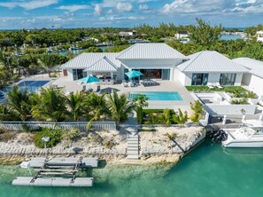 A modern beachfront property with a large pool, outdoor seating, and a boat dock. - Turks & Caicos Waterfront Villa, Pool, Private Dock & Pickleball (Leeward Settlement)