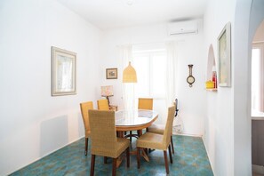 Comedor con una mesa redonda, sillas de mimbre, lámpara colgante y baldosas de suelo estampadas.