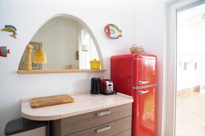 Una cocina con un refrigerador rojo, una tabla de cortar de madera, una tetera y un tostador.