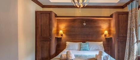 A hotel room with a large bed, wooden headboard, two bedside lamps, and a decorative ceiling light.