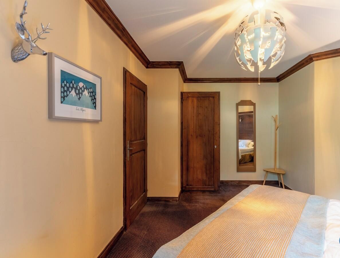 Une chambre d’hôtel avec un lit, une porte en bois, un tableau encadré au mur et un lustre.