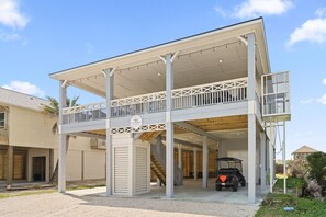 A covered outdoor area with a balcony, a staircase, and a vehicle parked inside. - Golf Cart, Elevator, Stylish, 12 guests - LaPerla (Bolivar Peninsula)