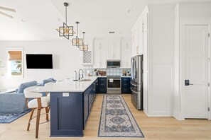 A modern kitchen with white cabinets, a central island, stainless steel appliances, and a patterned rug. - Golf Cart, Elevator, Stylish, 12 guests - LaPerla (Bolivar Peninsula)