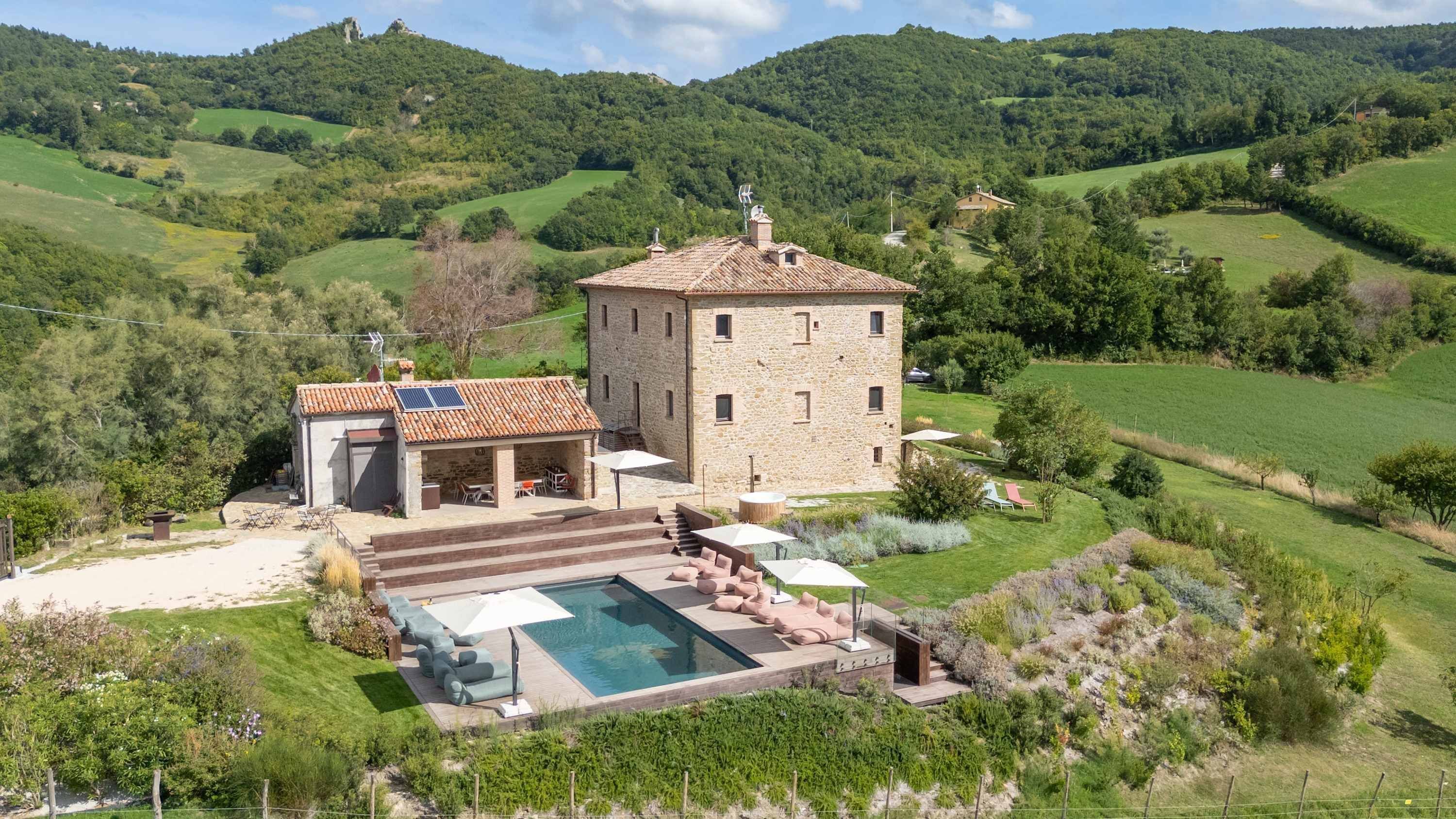 Una villa de piedra con piscina, mobiliario exterior y vistas a las colinas circundantes.