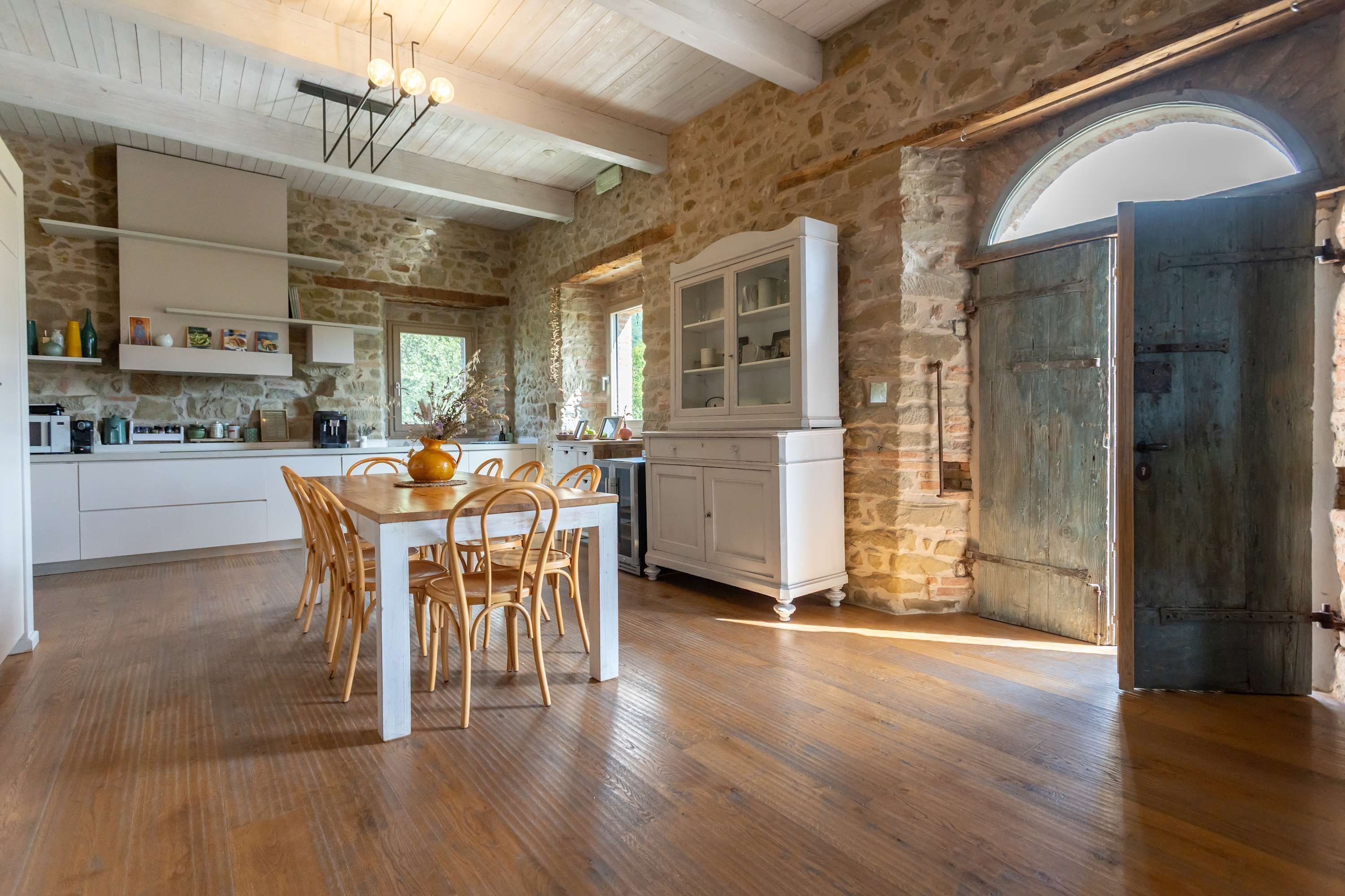 Una cocina rústica con paredes de piedra, suelo de madera y un comedor con mesa y sillas.