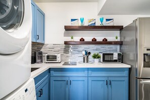 A modern kitchen with blue cabinets, a stainless steel refrigerator, a microwave, a toaster, and a washing machine.