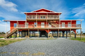 A two-story building with a balcony on the upper level, a covered front porch, and a gravel driveway. - Cozy 2BR beach stay with a kitchenette—just a short walk to the sand. (Bolivar Peninsula)