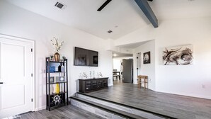 A spacious living area with a dark wood floor, a black entertainment unit, and a staircase leading to another level. - Cozy 2BR beach stay with a kitchenette—just a short walk to the sand. (Bolivar Peninsula)