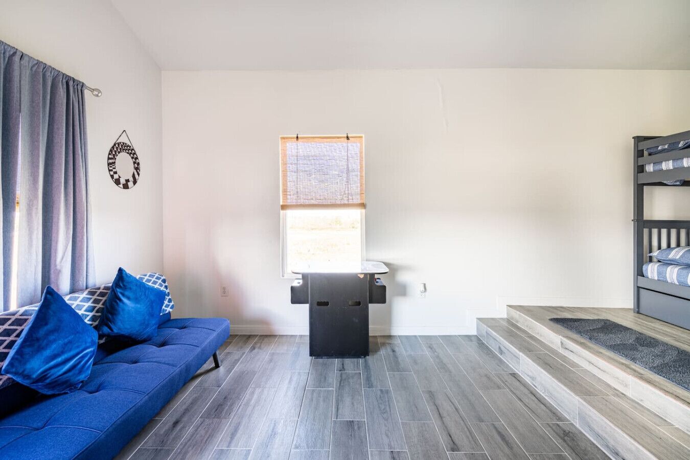 Habitació petita i moderna amb un sofà blau, una taula petita i un llit superposat.