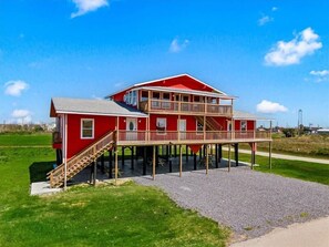 A two-story red house with a balcony, a staircase, and a gravel driveway.