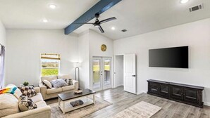 A spacious living room with a sofa, coffee table, and a flat-screen TV mounted on the wall. - Cozy 2BR beach stay with a kitchenette—just a short walk to the sand. (Bolivar Peninsula)