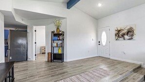 A spacious living room with a wooden floor, a black bookshelf, a white door, and a painting on the wall. - Cozy 2BR beach stay with a kitchenette—just a short walk to the sand. (Bolivar Peninsula)