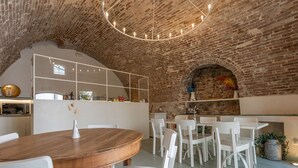 Un interior rústico con paredes de ladrillo visto, una mesa de comedor de madera, sillas blancas y una lámpara de araña moderna.