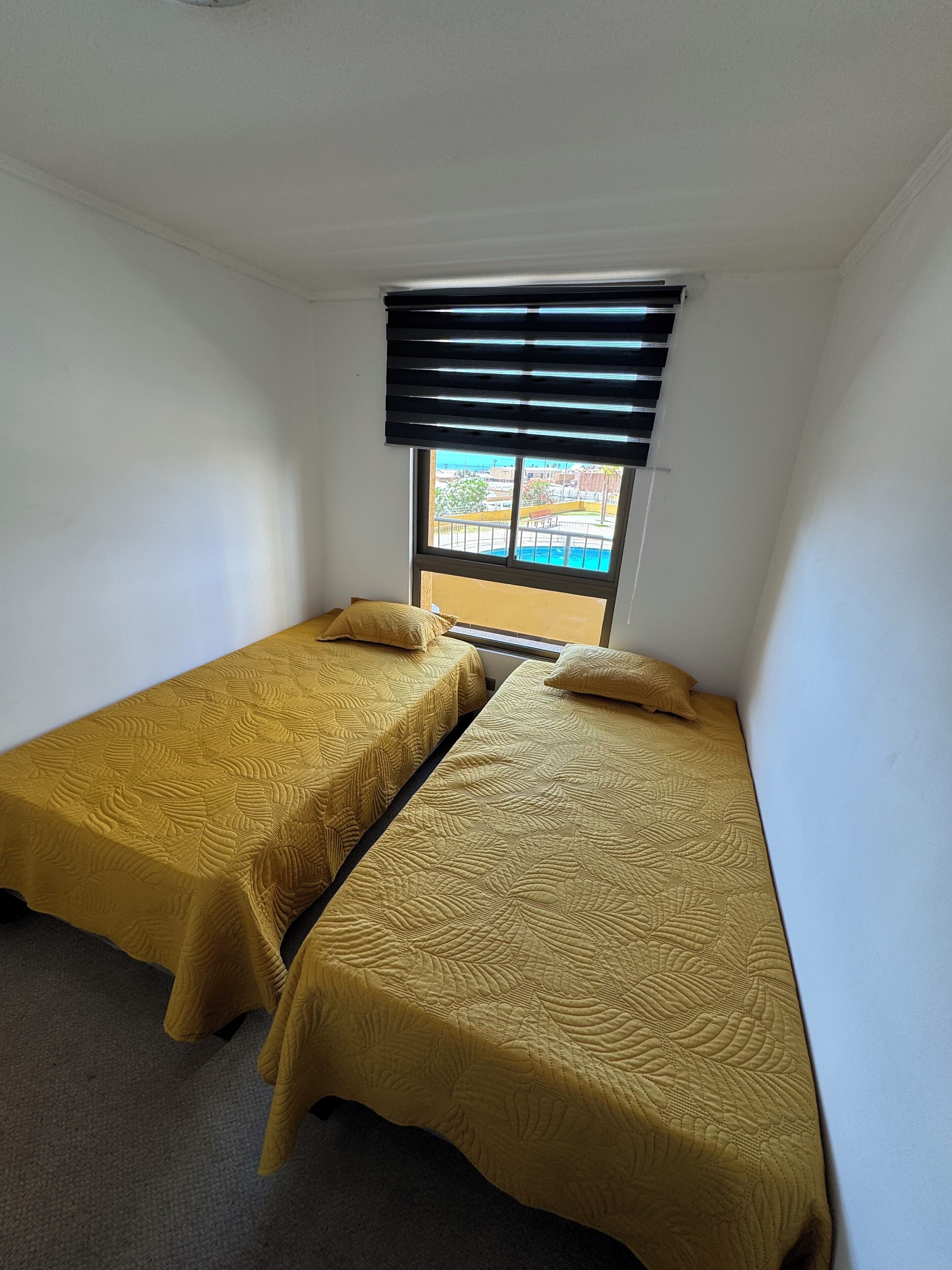 Une petite chambre avec deux lits simples, une fenêtre avec des stores et une vue sur une piscine.