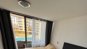 Hotellihuone, jossa on kaksi sänkyä, näköala uima-altaalle ja parveke, jossa on verhot.