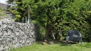 Un muro de piedra con una valla metálica, un árbol y una silla de plástico en una zona cubierta de hierba.