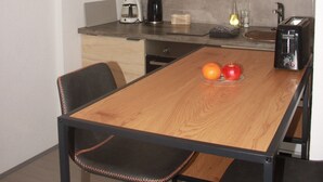 A modern kitchen with a wooden table, black chairs, a coffee maker, a toaster, and a TV above the counter.