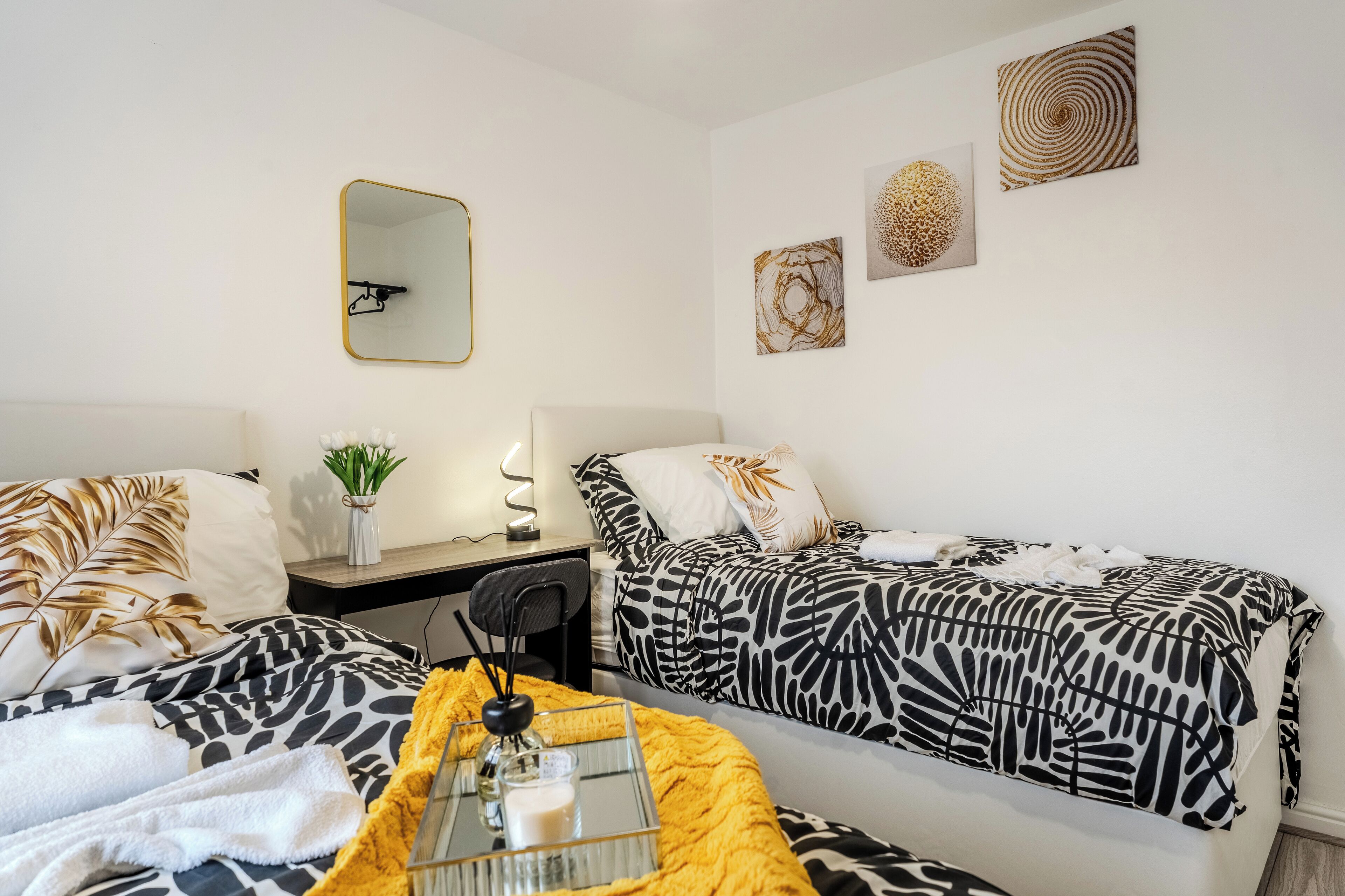 Une chambre d’hôtel avec deux lits, un bureau, une chaise, un miroir et des œuvres d’art accrochées aux murs.