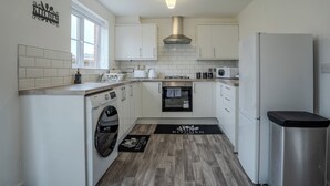 Una cocina compacta con armarios blancos, una campana extractora de acero inoxidable, horno empotrado, lavadora y refrigerador.