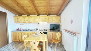 A kitchen with wooden cabinets, a dining table with chairs, a TV, and a radiator.