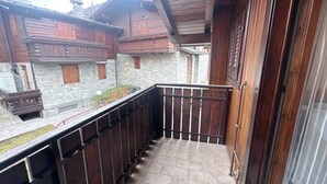 A balcony with stone walls and wooden shutters, leading to a stone building with a wooden balcony.