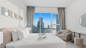 Une chambre d’hôtel moderne dotée d’un grand lit, d’un coin salon et offrant une vue sur le paysage urbain grâce à de grandes fenêtres du sol au plafond.
