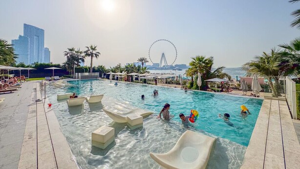 Une piscine avec des chaises longues et des parasols, une grande roue en arrière-plan et une vue sur les gratte-ciel de la ville.