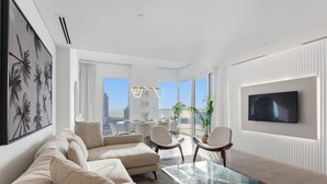 Un salon moderne avec une table basse en verre, des canapés de couleur beige et un téléviseur à écran plat fixé au mur.