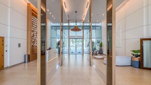 Un hall d’hôtel moderne doté d’un comptoir d’accueil, d’un espace salon et de murs en verre offrant une vue sur la rue.