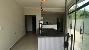 A modern kitchen with a central island, pendant lighting, and a glass door leading to an outdoor area. - Pousada Vila Palmital (Paraty)