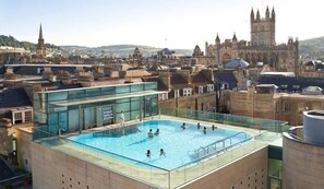 A rooftop swimming pool with a glass barrier, overlooking a historic cityscape with notable architecture. - Exquisite grandeur - Central Bath (Bath)
