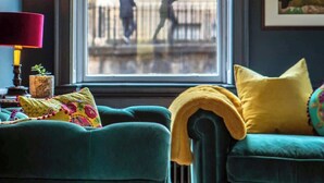 Ein Zimmer mit einem großen Fenster, einem grünen Sofa, einem gelben Kissen und einer roten Lampe.