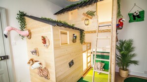 A children's playroom with a wooden playhouse, climbing wall, and various stuffed animals. - Le Savannah (Saint-Aignan)