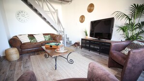 A living room with a brown leather sofa, a coffee table, a TV, and a staircase. - Le Savannah (Saint-Aignan)
