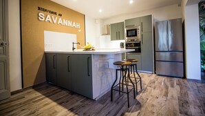 A modern kitchen with a central island, bar stools, a stainless steel refrigerator, and a wall-mounted oven. - Le Savannah (Saint-Aignan)
