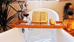 A bathtub with a wooden tray holding a book and a glass of wine, surrounded by plants and a lit candle. - Le Savannah (Saint-Aignan)