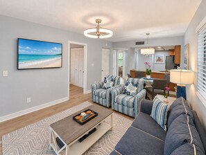 Ein modernes Wohnzimmer mit Fernseher, Sofas, einem Couchtisch und einer Küchenzeile im Hintergrund.