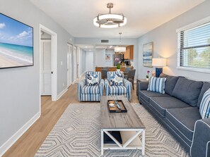 Een moderne woonkamer met een bank, fauteuils, een salontafel en een eethoek, met een keuken op de achtergrond.