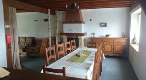 A dining area with a long table, wooden chairs, a fireplace, and a kitchen area with wooden cabinets.